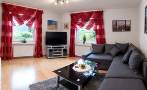 A living room with a sofa, a coffee table, a TV, and red curtains.