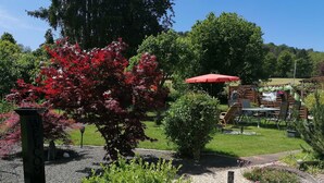 A garden with a red umbrella, a welcome sign, and a variety of plants.