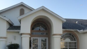 Une maison à deux étages, dotée d’une façade symétrique, d’une entrée centrale en arc de cercle et d’une allée carrossable pavée.
