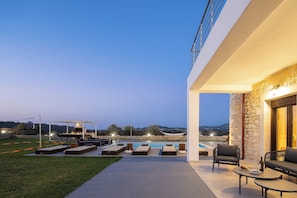 An outdoor patio with lounge chairs, a pool, and a stone wall.