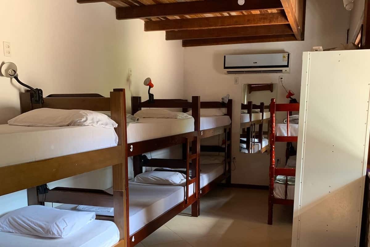 A dormitory room with bunk beds, a ceiling fan, an air conditioning unit, and a small kitchenette area.