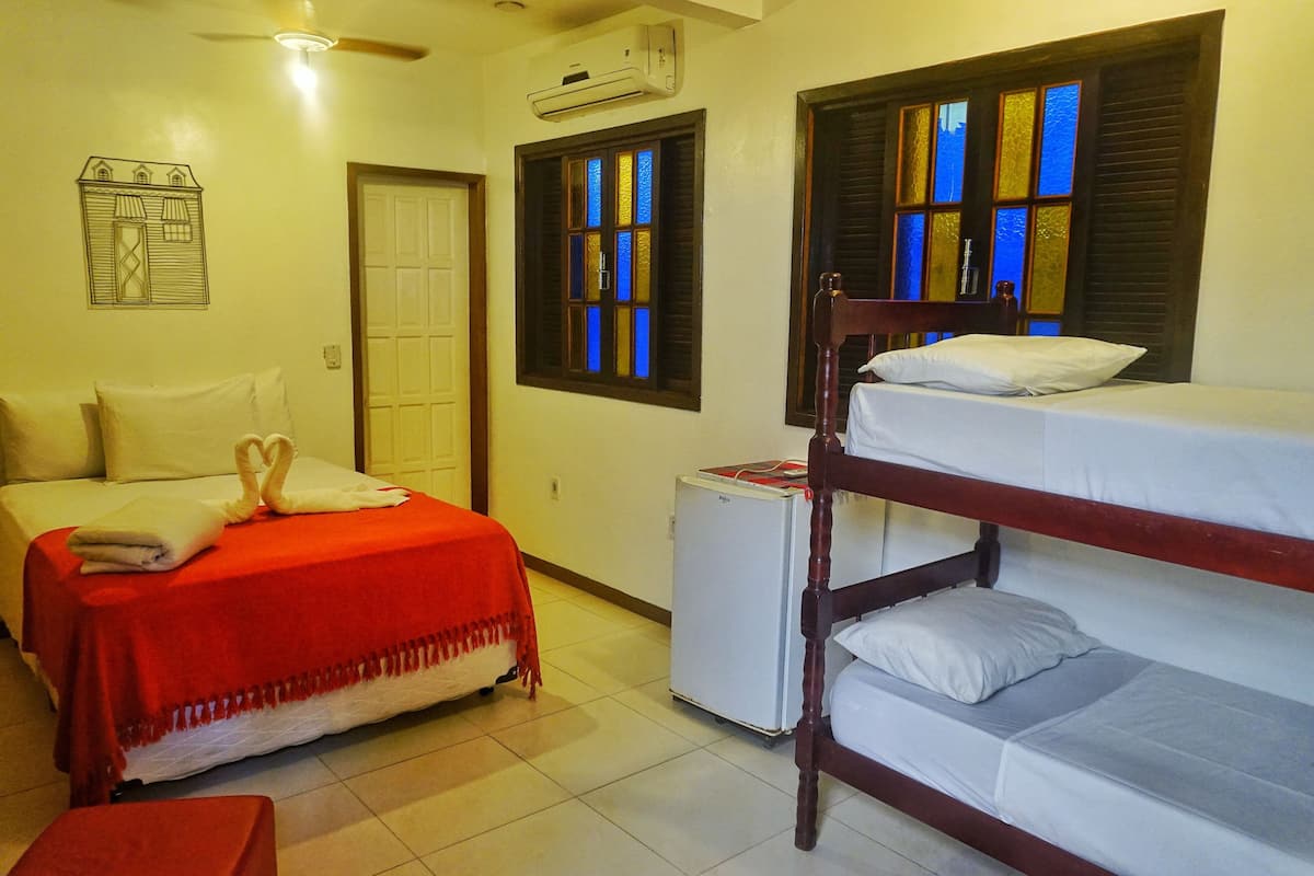 A room with a single bed, a bunk bed, a small refrigerator, and a window with stained glass.