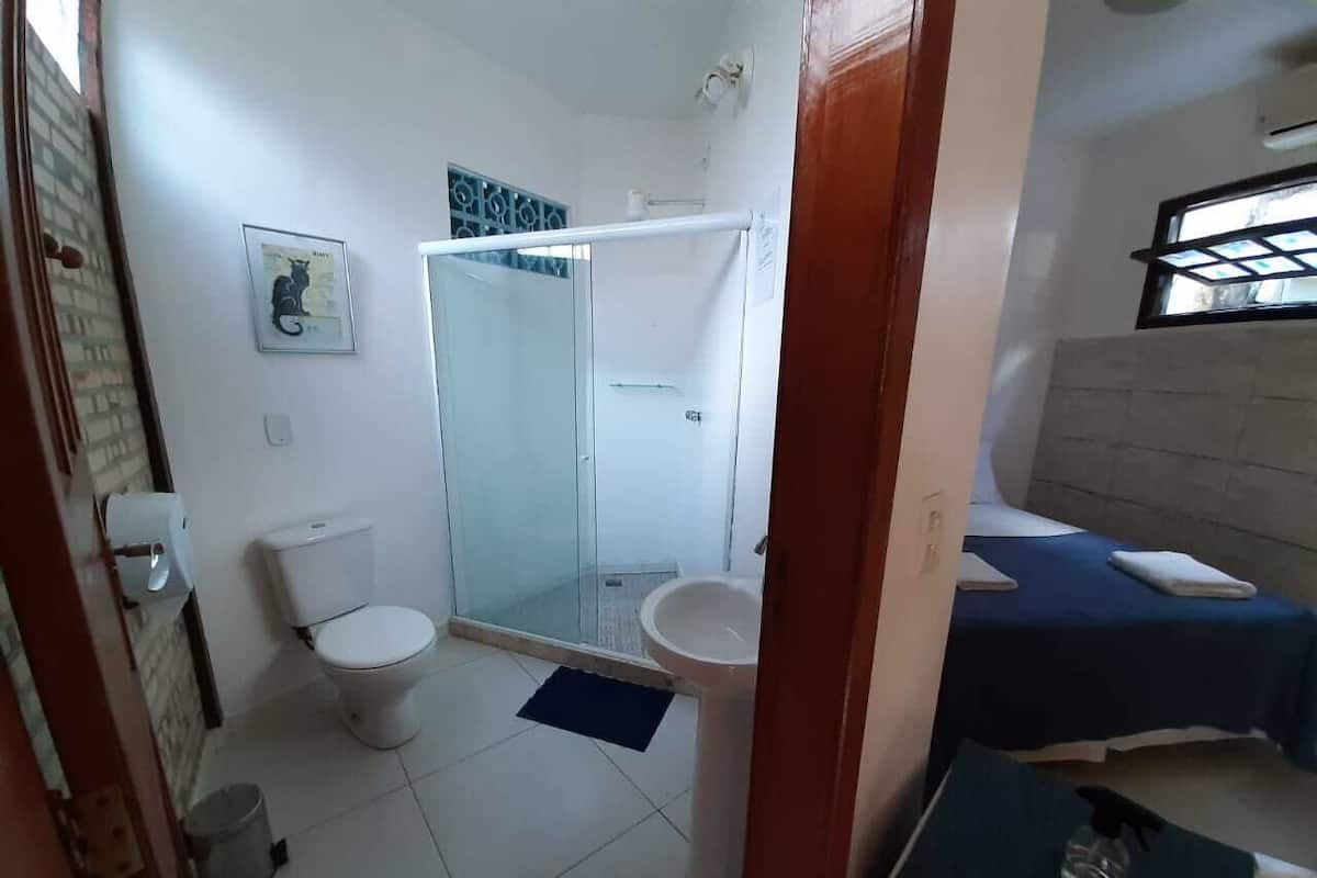 A bathroom with a toilet, sink, and shower. There is a small rug on the floor and a towel on the counter.