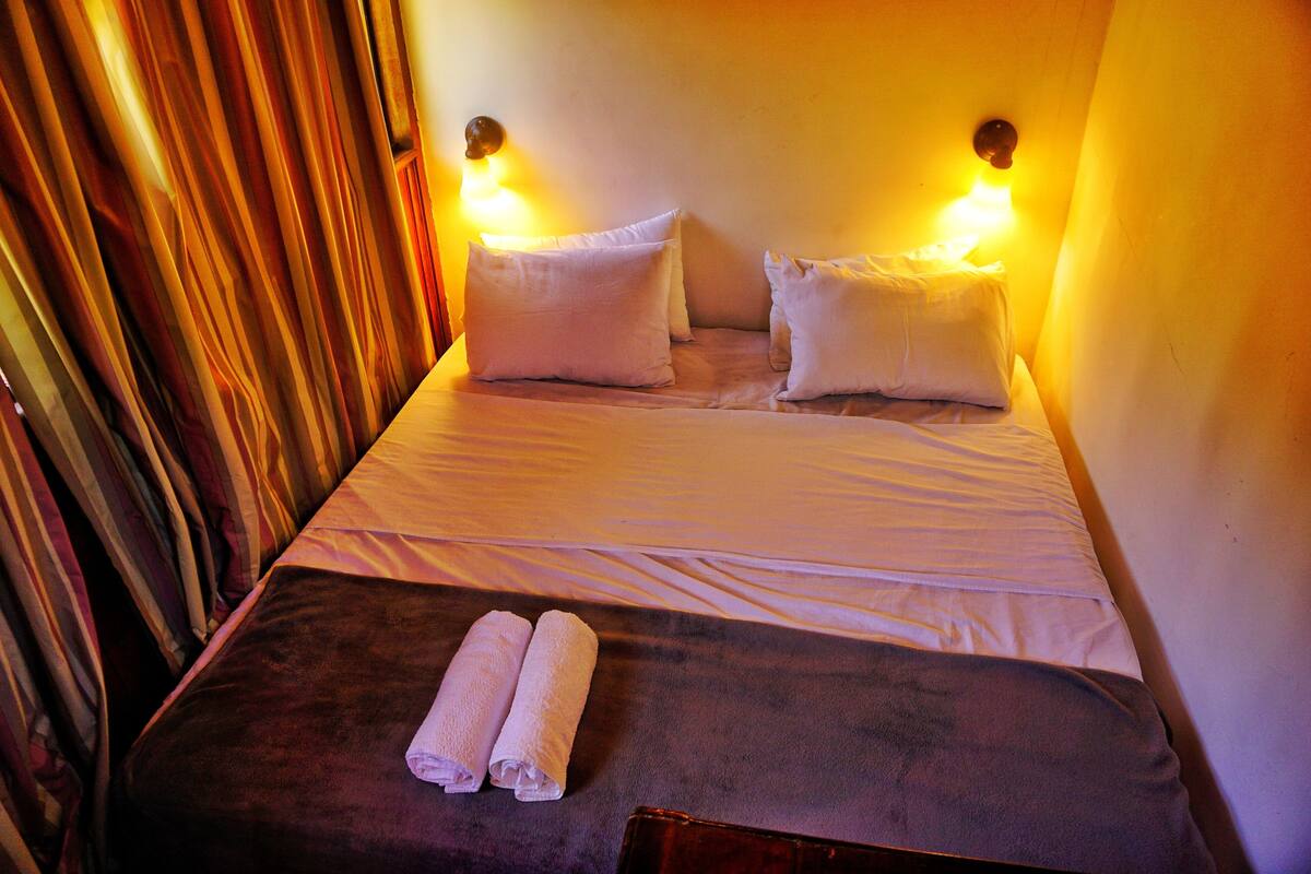 A hotel room with a bed, two pillows, a blanket, and two towels.