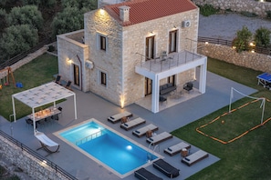 A stone house with a swimming pool, outdoor seating, and a tennis court.