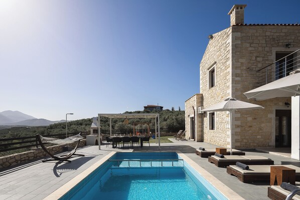 A poolside area with a stone building, outdoor seating, and a view of the landscape. - Dimokritos Villa VI, Family Stay with Lawn & Play (Aggeliana, Rethymno)