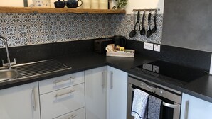 A modern kitchen with white cabinets, a black countertop, a built-in oven, and a backsplash with a blue and white pattern. - Seacot Cottage in the heart of the Highlands (Clachnaharry)