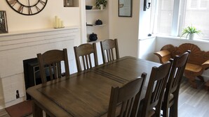 A dining area with a wooden table and chairs, a clock, and a fireplace. - Seacot Cottage in the heart of the Highlands (Clachnaharry)