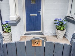 A blue door with a number 9 plaque, flanked by potted plants with blue flowers. - Seacot Cottage in the heart of the Highlands (Clachnaharry)
