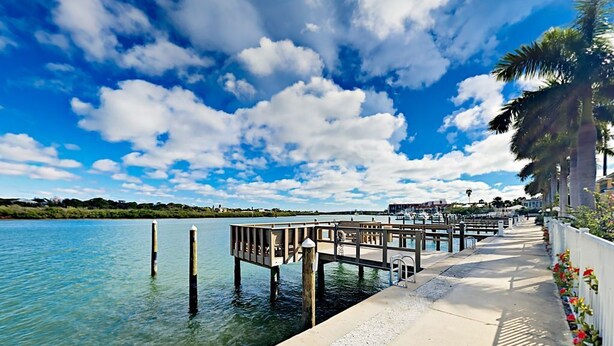 A waterfront pier with a concrete walkway, palm trees, and a clear blue sky.