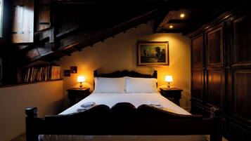 A dimly lit bedroom with a wooden bed, two bedside lamps, a painting on the wall, and a bookshelf with books.