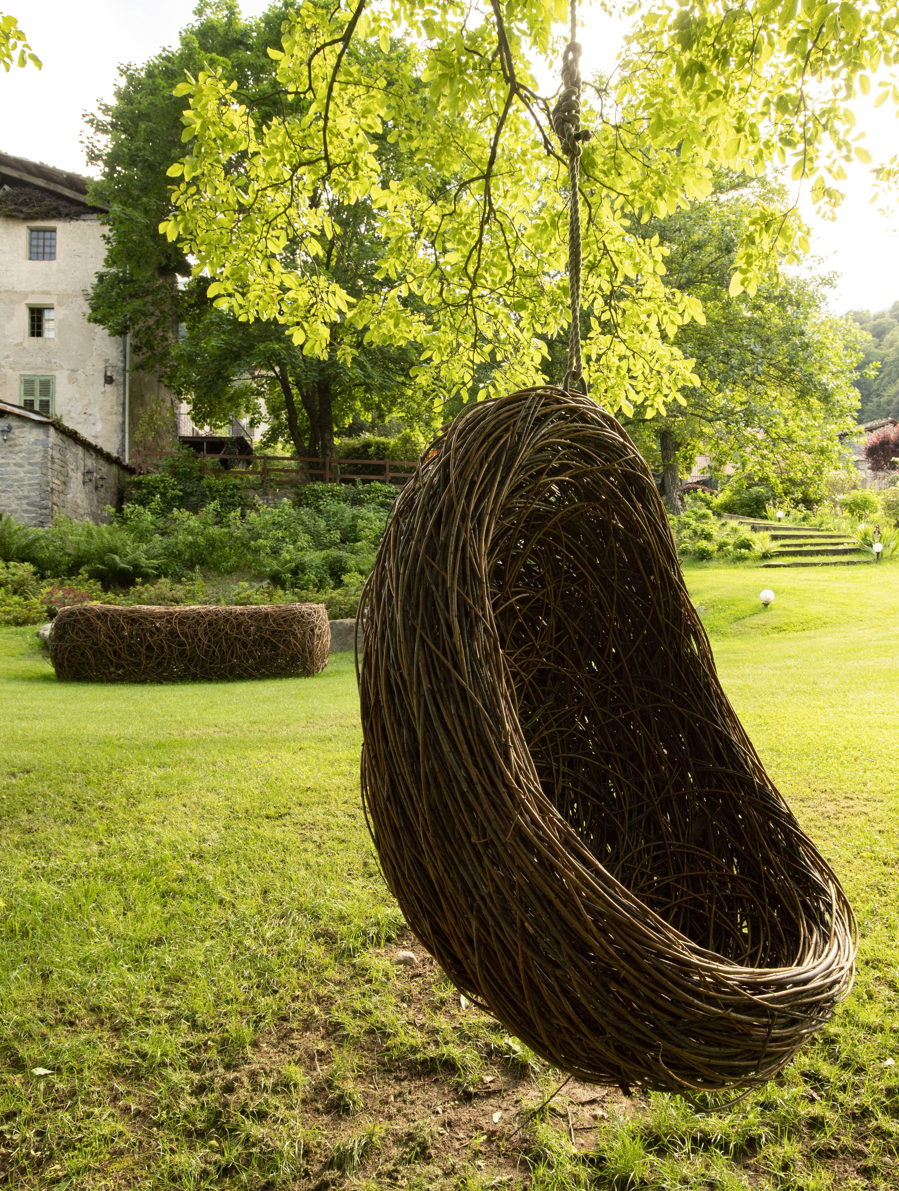 A wicker hanging chair in a lush garden with a stone building in the background.