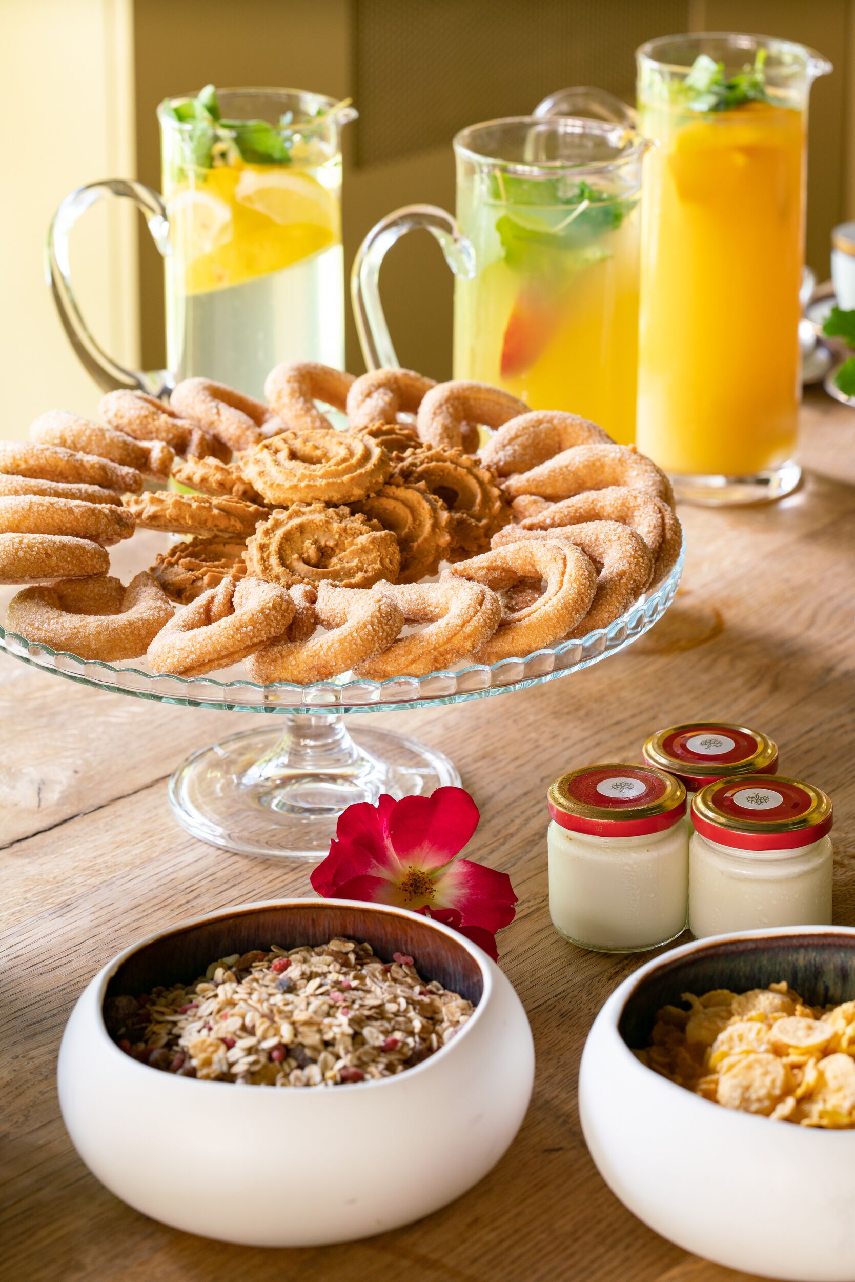 Ein Tisch mit einer Glaskuchenvorrichtung, die ein spiralförmiges Gebäck trägt, zwei Karaffen mit fruchtigen Getränken und Schüsseln mit Müsli.