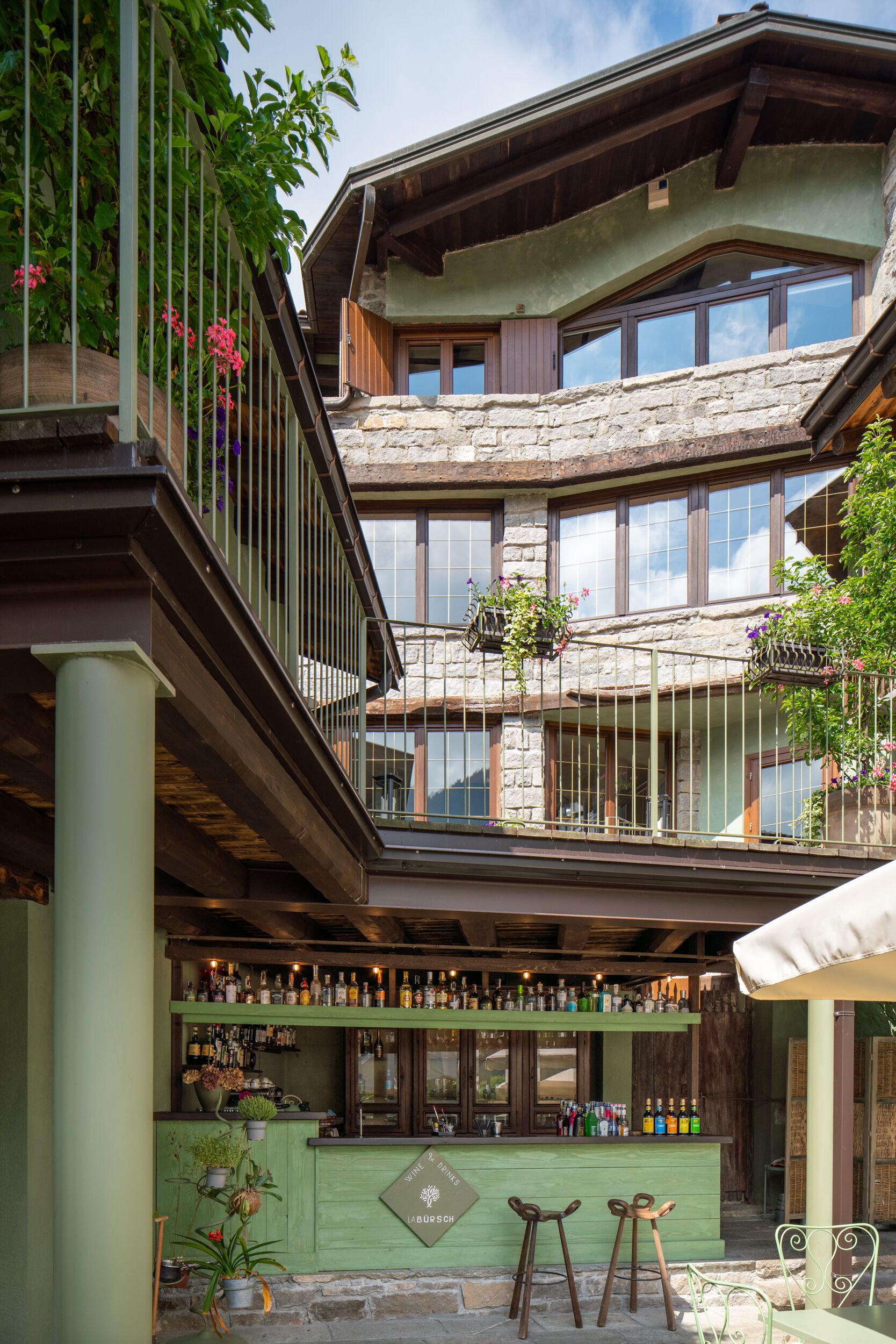 Un edificio a più piani con un'area bar al piano terra, pareti in pietra e balconi decorati con cesti di fiori.