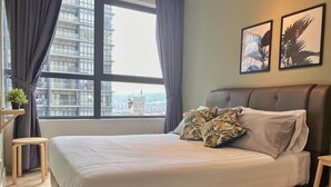 A neatly made bed with a white comforter and patterned pillows, a small wooden stool, and a view of a cityscape through a large window with curtains. - ARTE PLUS - COZY & COMFORTABLE (PVT LIFT)  (Kuala Lumpur)