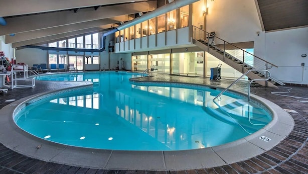 An indoor swimming pool with a central staircase and lounge chairs. - Classic Cabin in Pocono Mountain Resort (Gouldsboro)