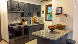 A kitchen with dark cabinets, a granite countertop, a stove, and a small island with stools. - Classic Cabin in Pocono Mountain Resort (Gouldsboro)