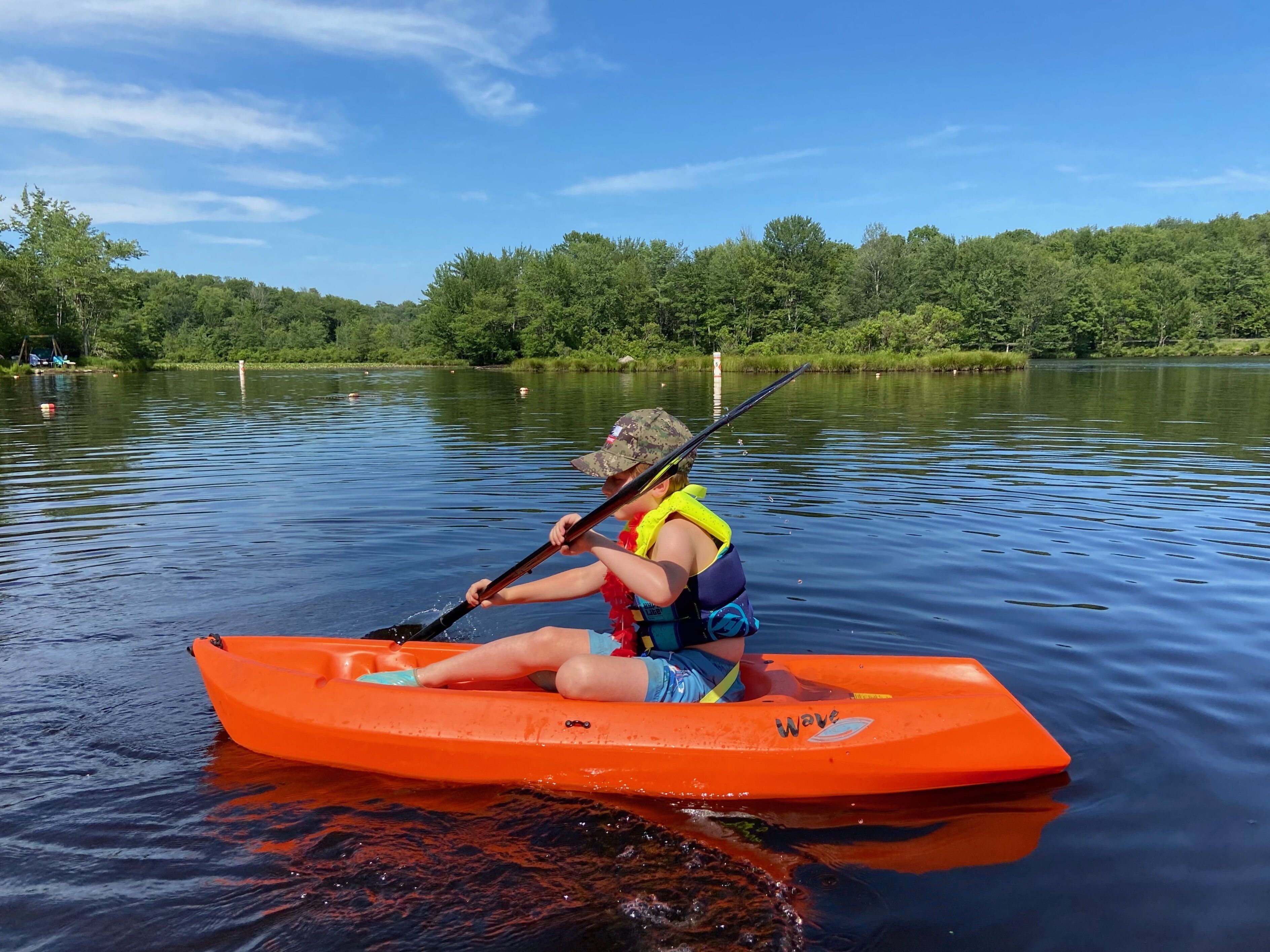 A person in an orange kayak on a calm lake with trees in the background.
