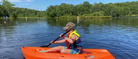 A person in an orange kayak on a calm lake with trees in the background.