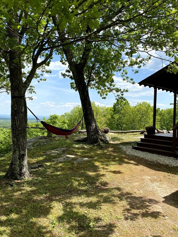 A hammock between two trees, a wooden gazebo, and a grassy area with a view of the landscape.
