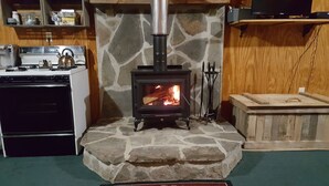 Una chimenea de piedra con un horno negro, un armario de madera y una zona de cocina con horno y hervidor.