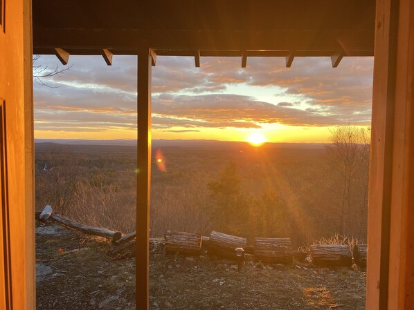 Vista attraverso una struttura in legno con un tramonto sullo sfondo, panchine e un paesaggio.