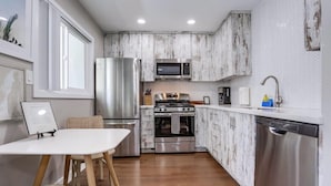A compact kitchen with a refrigerator, microwave, stove, oven, and dishwasher. There is a dining table with chairs and a window above it.