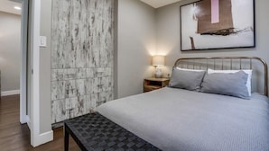 A bedroom with a bed, a nightstand, a lamp, a ceiling fan, and a wall-mounted abstract painting.