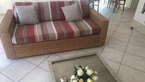 A wicker sofa with striped cushions, a small table with a vase of flowers, and a tiled floor. - Villa Senator-Marstall - stylish and close to the beach (Travemünde)