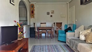 Un soggiorno con televisione, un tavolo da pranzo con sedie, un divano e un tappeto colorato.