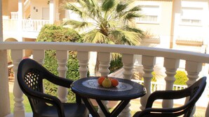 Un balcone con due sedie nere e un tavolino rotondo con un centrotavola di frutta.