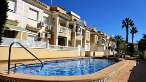 Una piscina con bordo piastrellato, circondata da un vialetto in mattoni e un recinto bianco.