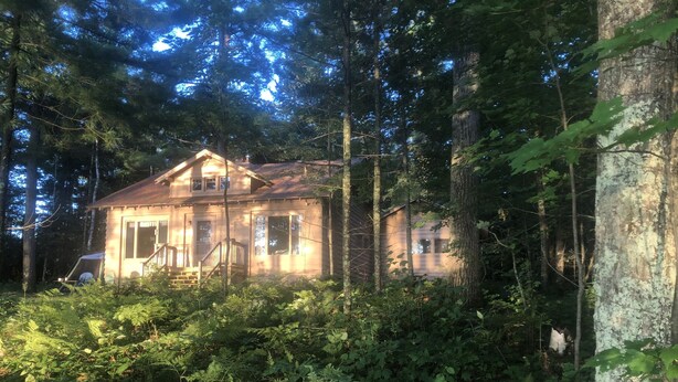 A rustic cabin surrounded by dense forest, with a wooden porch and a visible garage. - The Keith Farm Cabin, right on peaceful BIG Lake -48 acres!!! (Presque Isle)