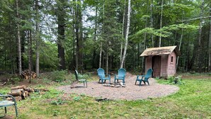 A rustic cabin with a small porch, surrounded by a forest. There are four Adirondack chairs arranged around a fire pit. - The Keith Farm Cabin, right on peaceful BIG Lake -48 acres!!! (Presque Isle)