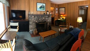 A cozy living room with a stone fireplace, a television, and wooden furniture. - The Keith Farm Cabin, right on peaceful BIG Lake -48 acres!!! (Presque Isle)