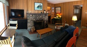 A cozy living room with a stone fireplace, a television, and wooden furniture. - The Keith Farm Cabin, right on peaceful BIG Lake -48 acres!!! (Presque Isle)