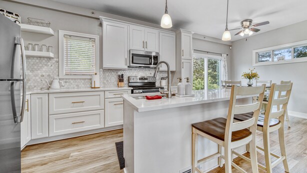 A modern kitchen with white cabinetry, a central island, a microwave, and a ceiling fan. - Minutes to the Beach, Douglas, & Saugatuck! (Douglas)