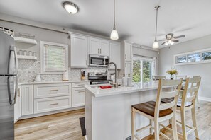 Une cuisine moderne avec des meubles blancs, un îlot central, un four à micro-ondes et un ventilateur de plafond.