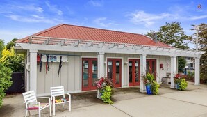 A building with a red roof and white exterior, featuring a covered patio area with white chairs and potted plants. - Minutes to the Beach, Douglas, & Saugatuck! (Douglas)