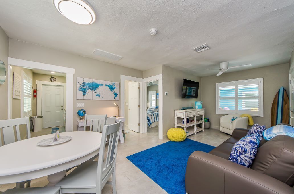 A spacious living area with a dining table, a sofa, and a TV. There are doors leading to other rooms, and a globe on the wall.