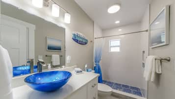 A bathroom with a large blue glass sink, a white toilet, a shower with a curtain, and a sign that says "RELAX LIFE IS GOOD".