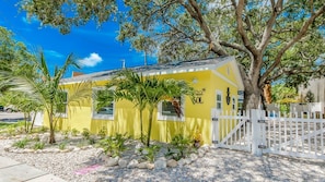 A yellow house with a white fence, surrounded by small plants and a large tree. - SOL Cottage, Best Experience in IRB, new AC, totally remodeled, free parking (Indian Rocks Beach)