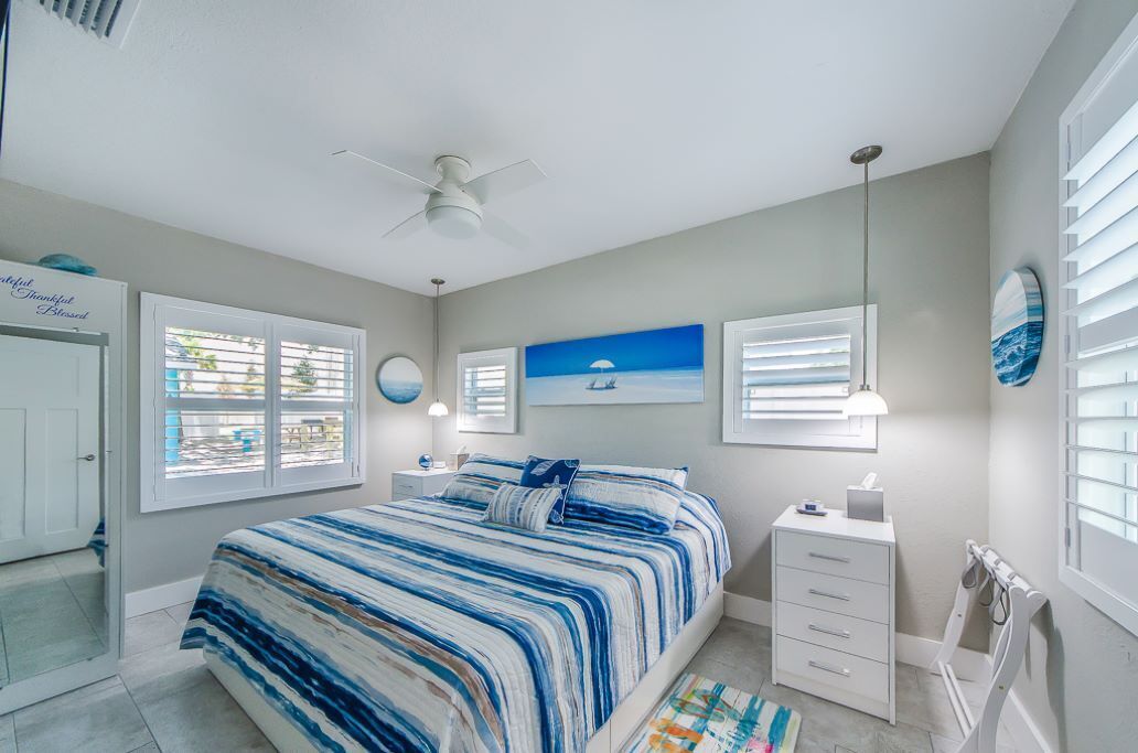 A bedroom with a bed, a nightstand, a desk, a chair, and a ceiling fan.