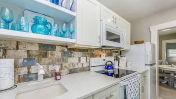 A kitchen with white cabinets, a microwave, a kettle, and a sink.