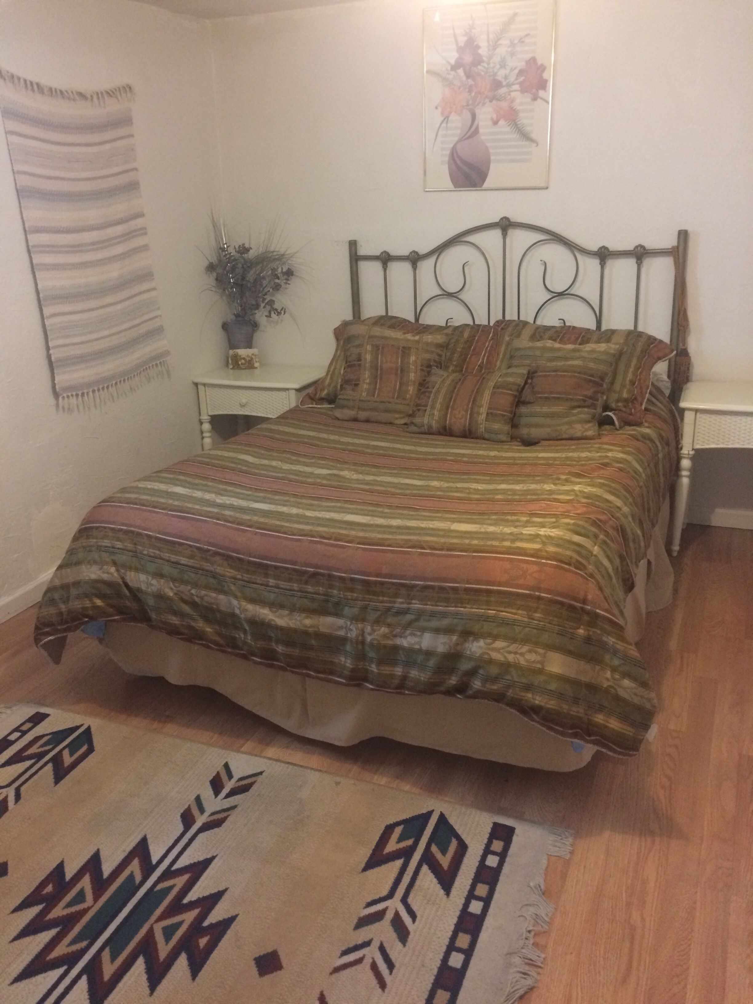 A bedroom with a bed, a nightstand, a wall hanging, and a rug.