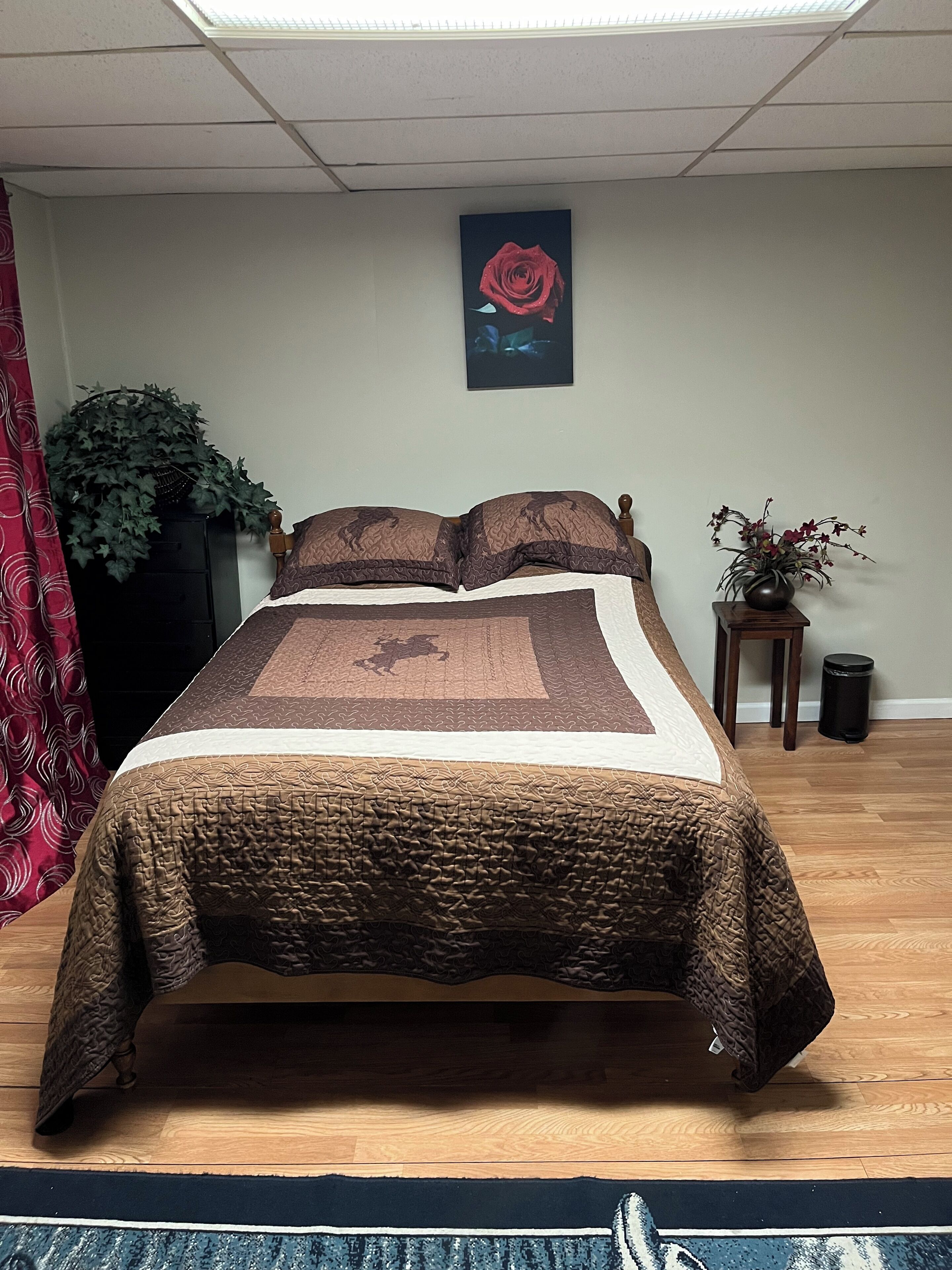 Un lit bien fait, recouvert d’une couvre-lit à motifs, avec une plante en pot et un tableau encadré accroché au mur.