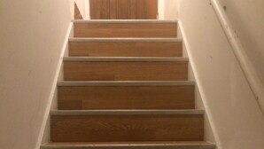 Una escalera de madera con paredes blancas y una puerta de madera en la parte superior.
