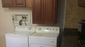 Un área de lavandería con dos secadoras blancas, armarios de madera arriba y un revoque de azulejos.