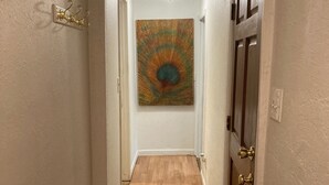 Un pasillo con suelo de madera, alfombra roja estampada, un cuadro en la pared y una puerta con pomo de latón.