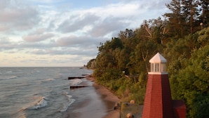 Paisaje costero con un faro de ladrillo rojo, un muelle de madera y abundante vegetación.